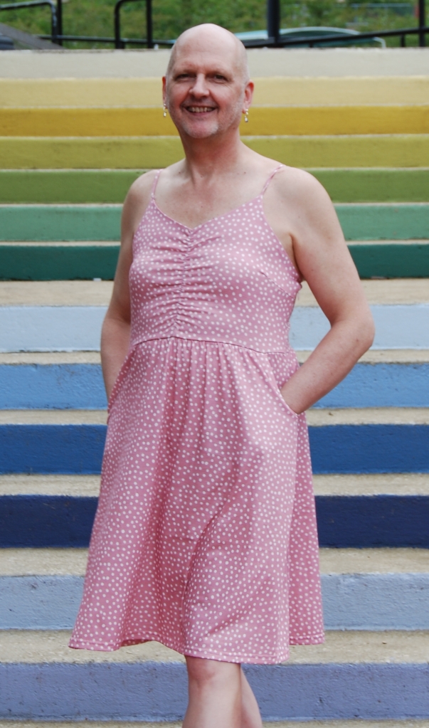 Danielle is standing on the stairs with her hands in the pockets of the pink sundress.